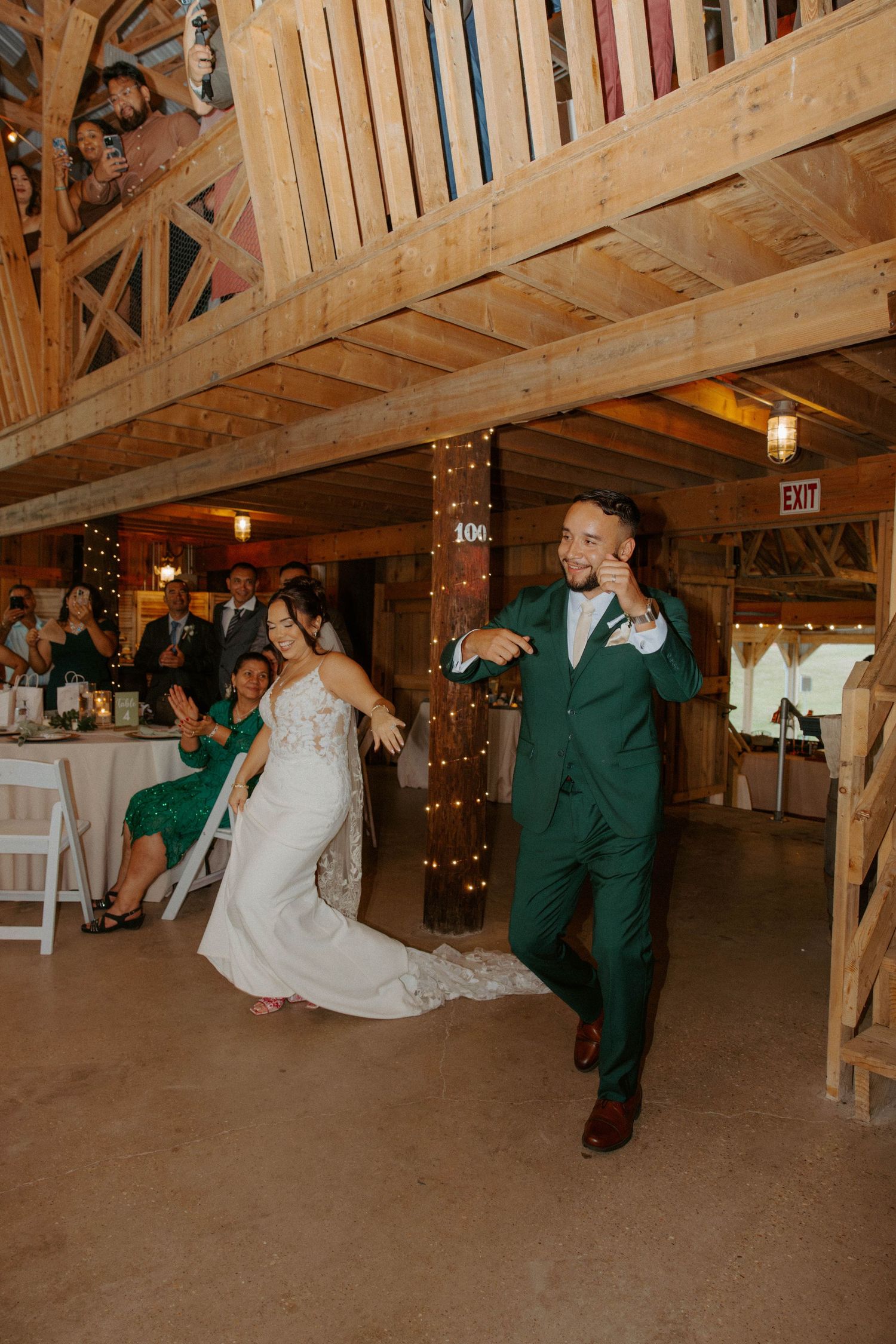 Bride and groom make grand entrance into rustic barn wedding reception, groom wearing green suit.