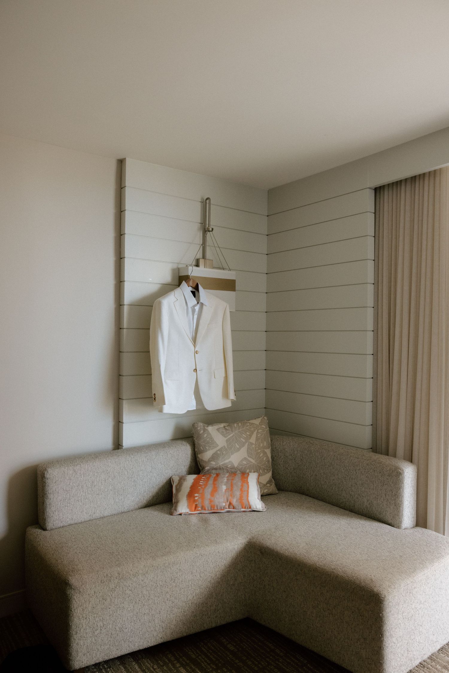 White suit jacket hanging on a wall-mounted rack above a modern neutral-toned sofa.