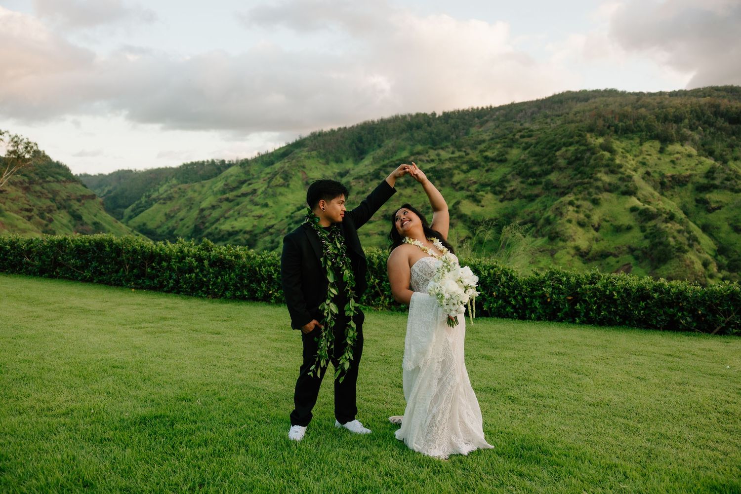 Bride and groom dancing on green lawn with lush Hawaiian mountain backdrop on their wedding day.