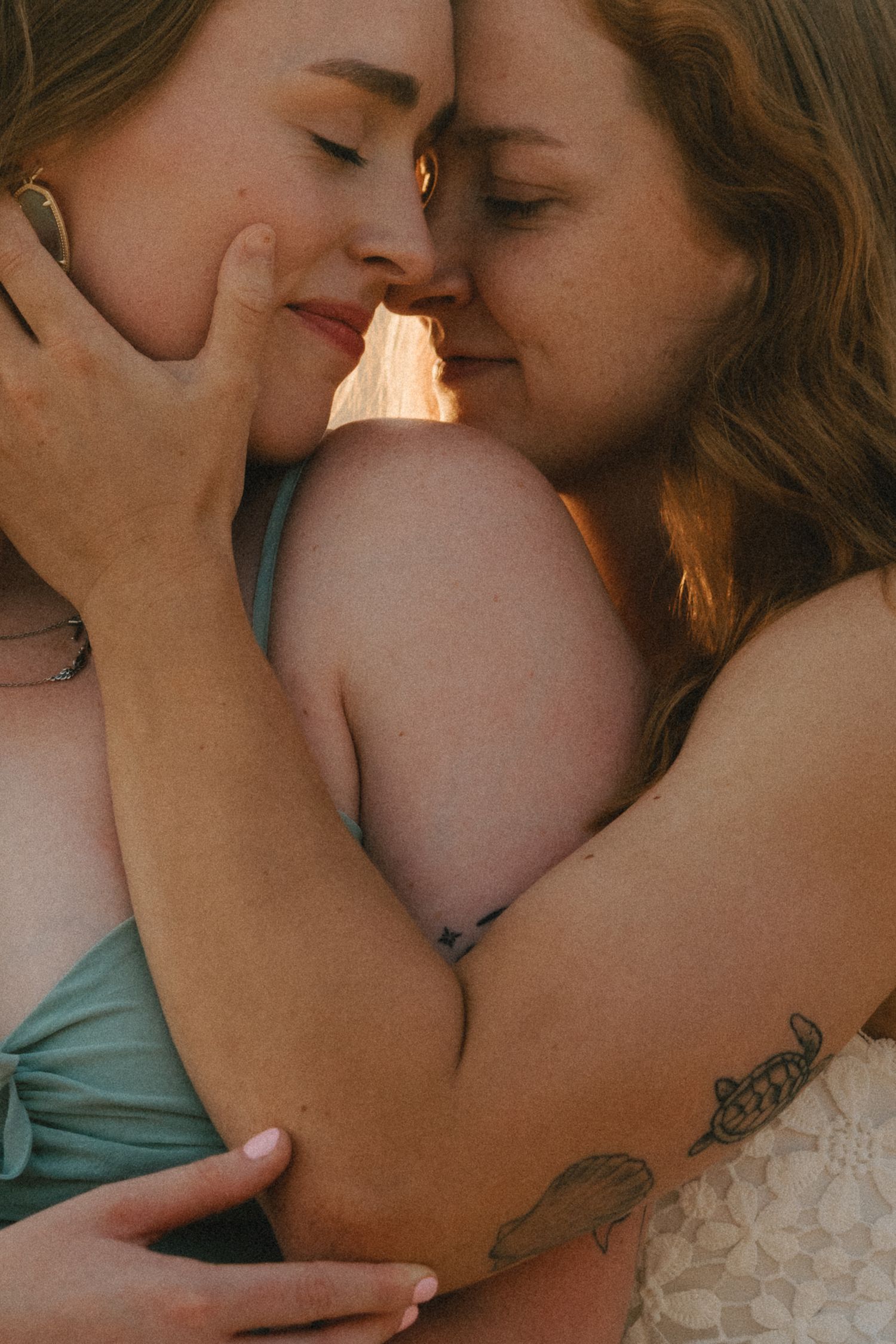 Two women sharing an intimate embrace, foreheads touching, with warm golden backlight in a tender romantic moment.