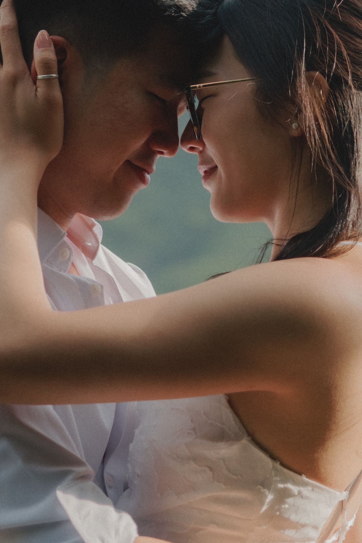Romantic couple sharing an intimate moment, foreheads touching, dressed in wedding attire outdoors.