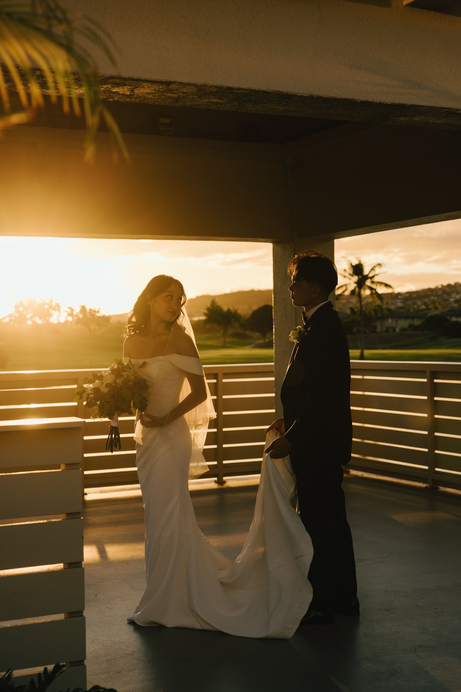 Bride and groom silhouetted in golden sunset light on covered outdoor venue terrace.