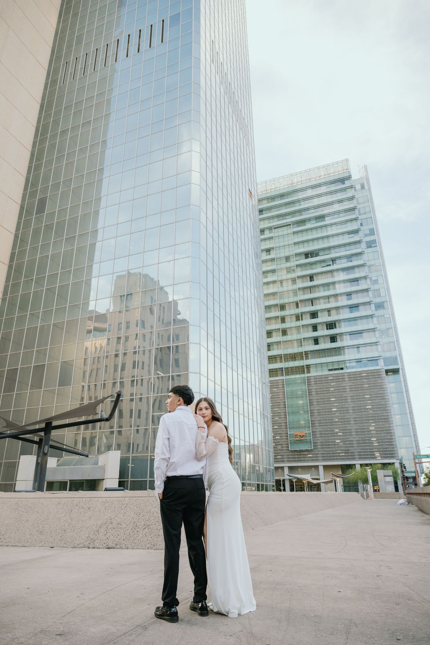 Wedding couple embracing in front of modern glass skyscrapers in an urban setting.