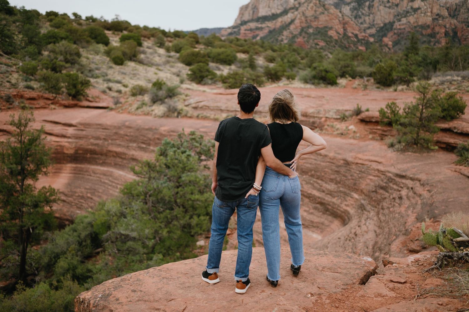 A couple stands together overlooking the red rocks of Sedona at sunset.