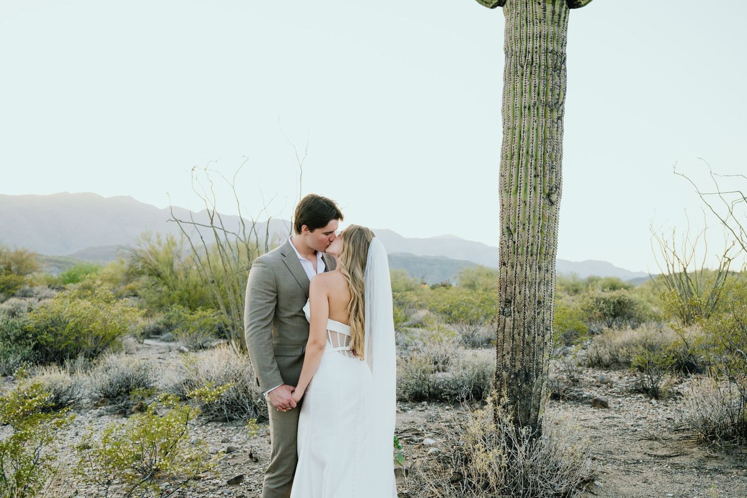 Wedding couple sharing an intimate moment beside a majestic saguaro cactus in the Arizona desert landscape.