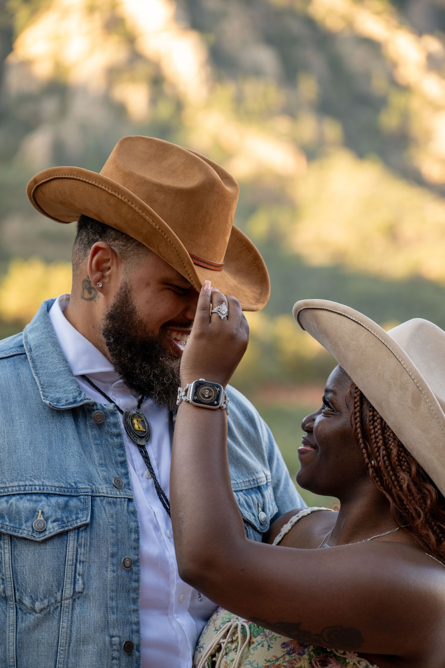 Two people in denim and cowboy hats share an intimate moment against a sunlit cliff backdrop.