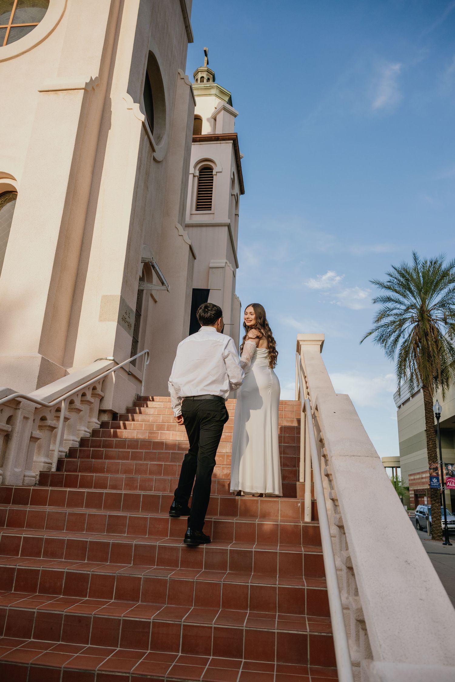 Couple ascending church steps in formal attire against Spanish colonial architecture.