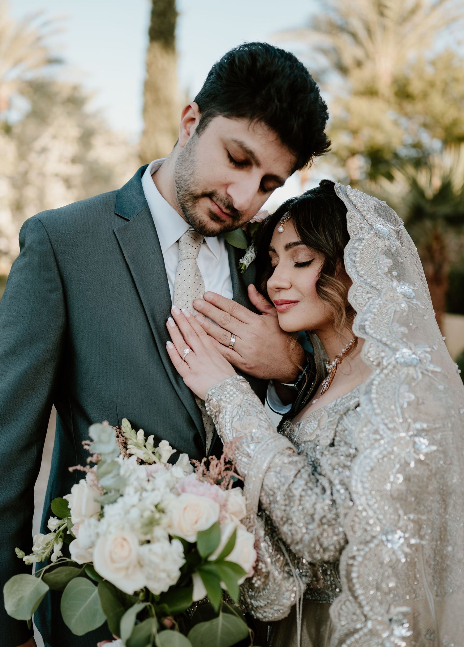 Newlyweds share an intimate moment outdoors with a beautiful wedding bouquet of white and pink flowers.