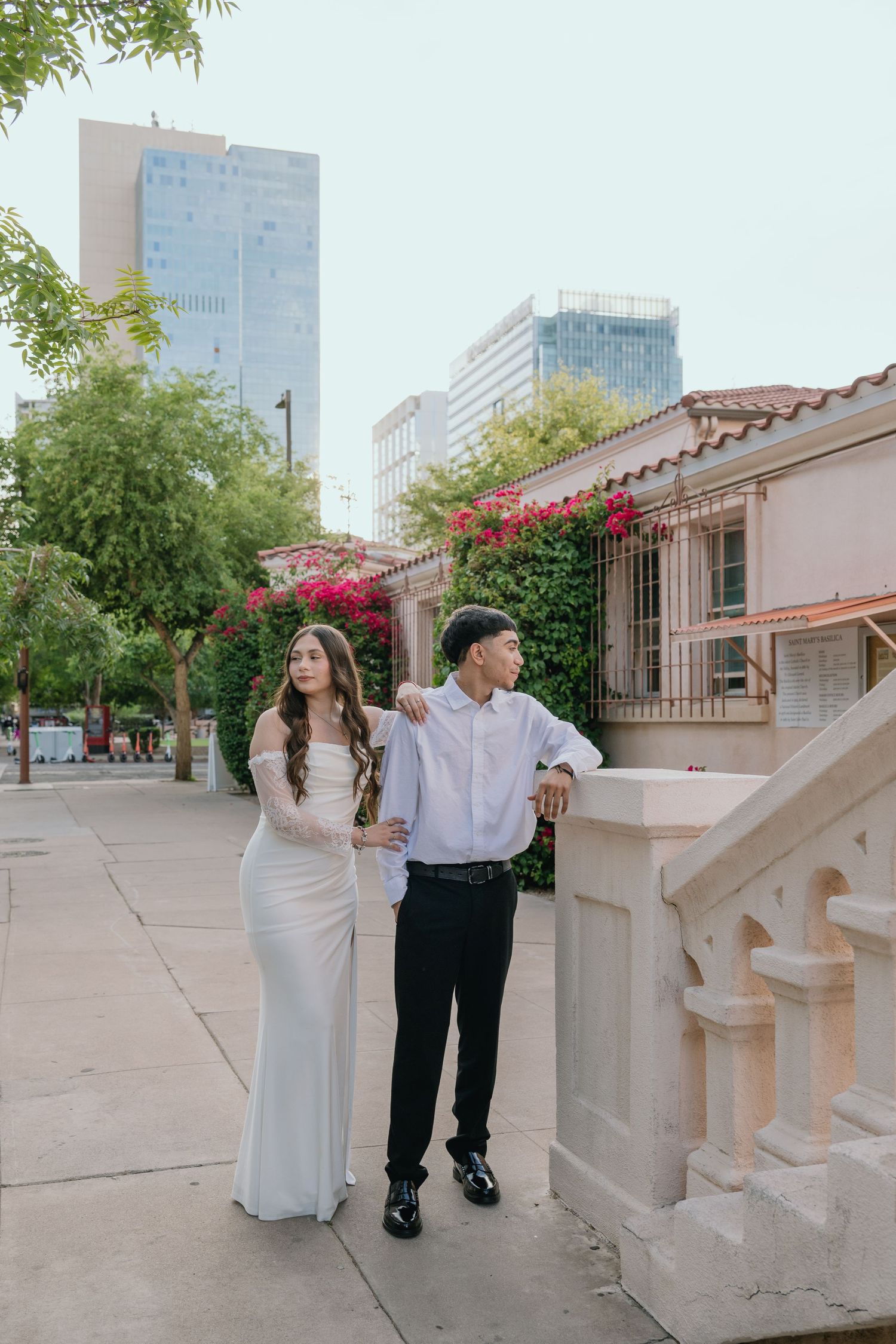 Elegant couple poses along a city sidewalk with Spanish colonial architecture and flowering bougainvillea.