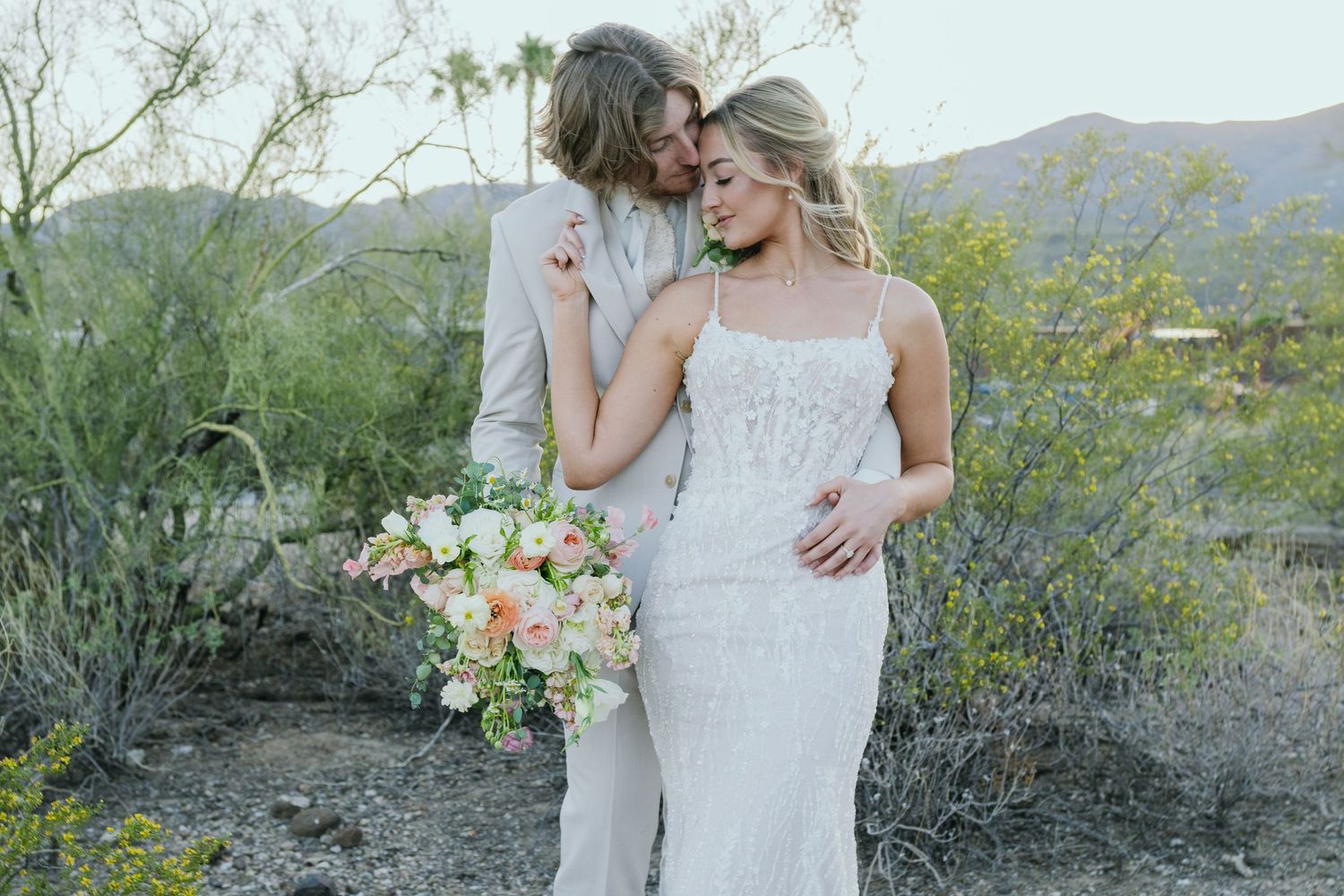 An intimate desert wedding portrait with soft lighting and a spring bouquet of pastel flowers.