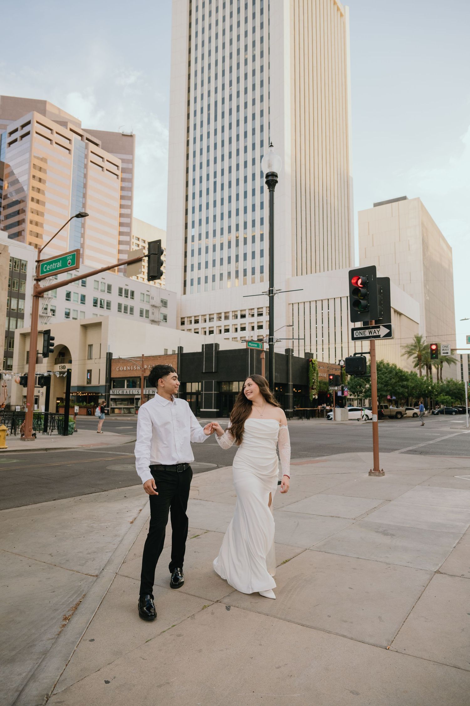 Couple walking hand in hand through city streets with tall buildings in background.