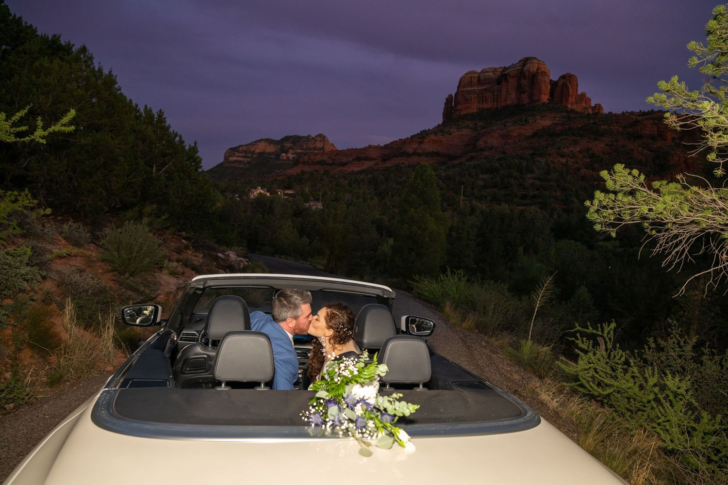 A convertible car parked at night with red rock formations of Sedona visible in the moonlit background.