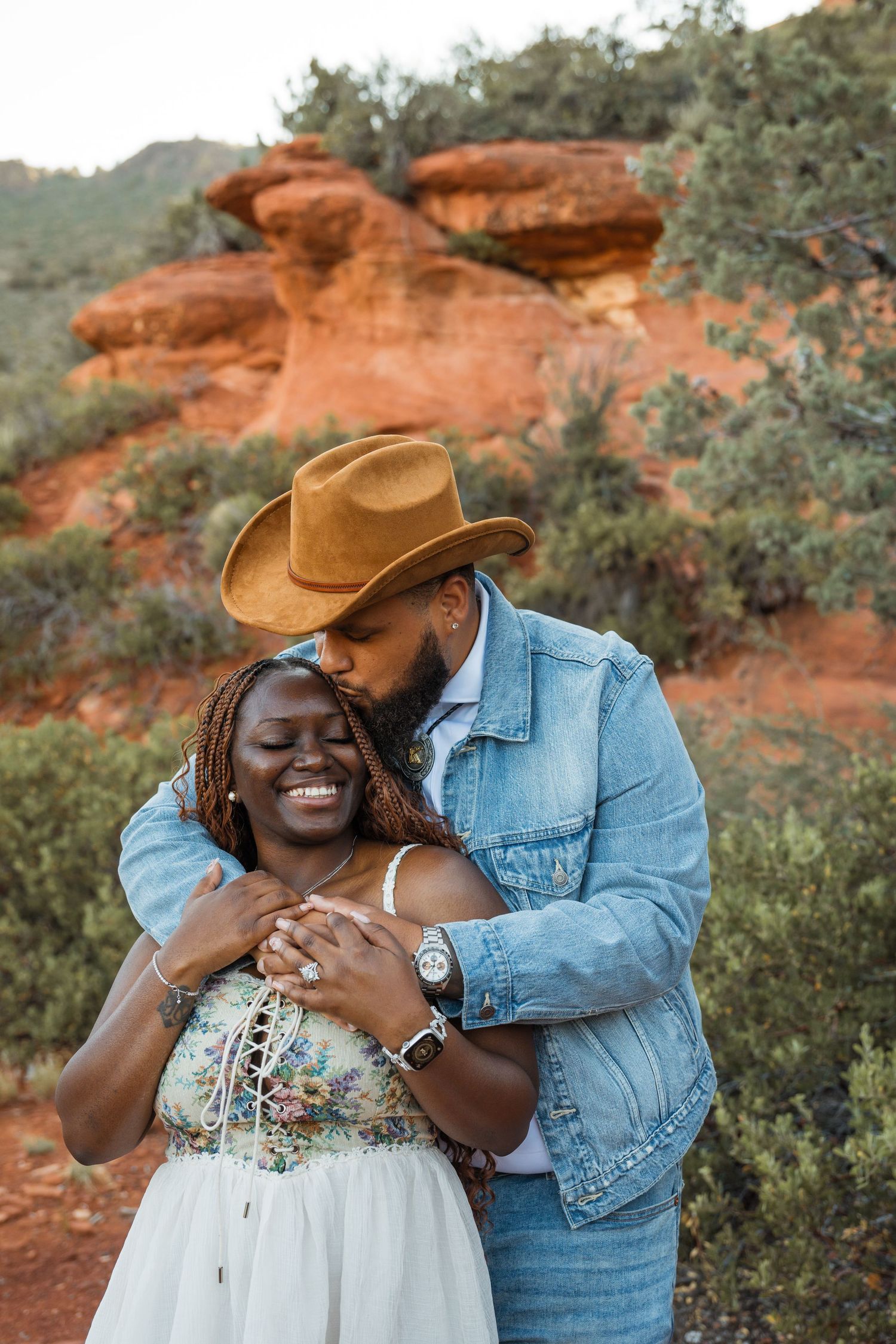 A couple shares joyful moments together against a backdrop of red rocks and desert vegetation in an outdoor photoshoot.