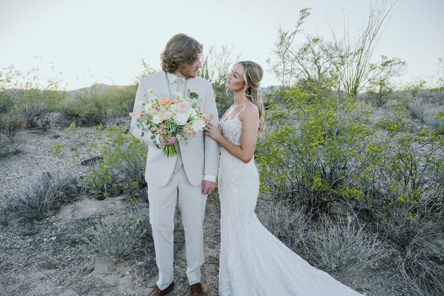 Two people share an intimate moment during their desert wedding ceremony surrounded by desert brush and wildflowers.
