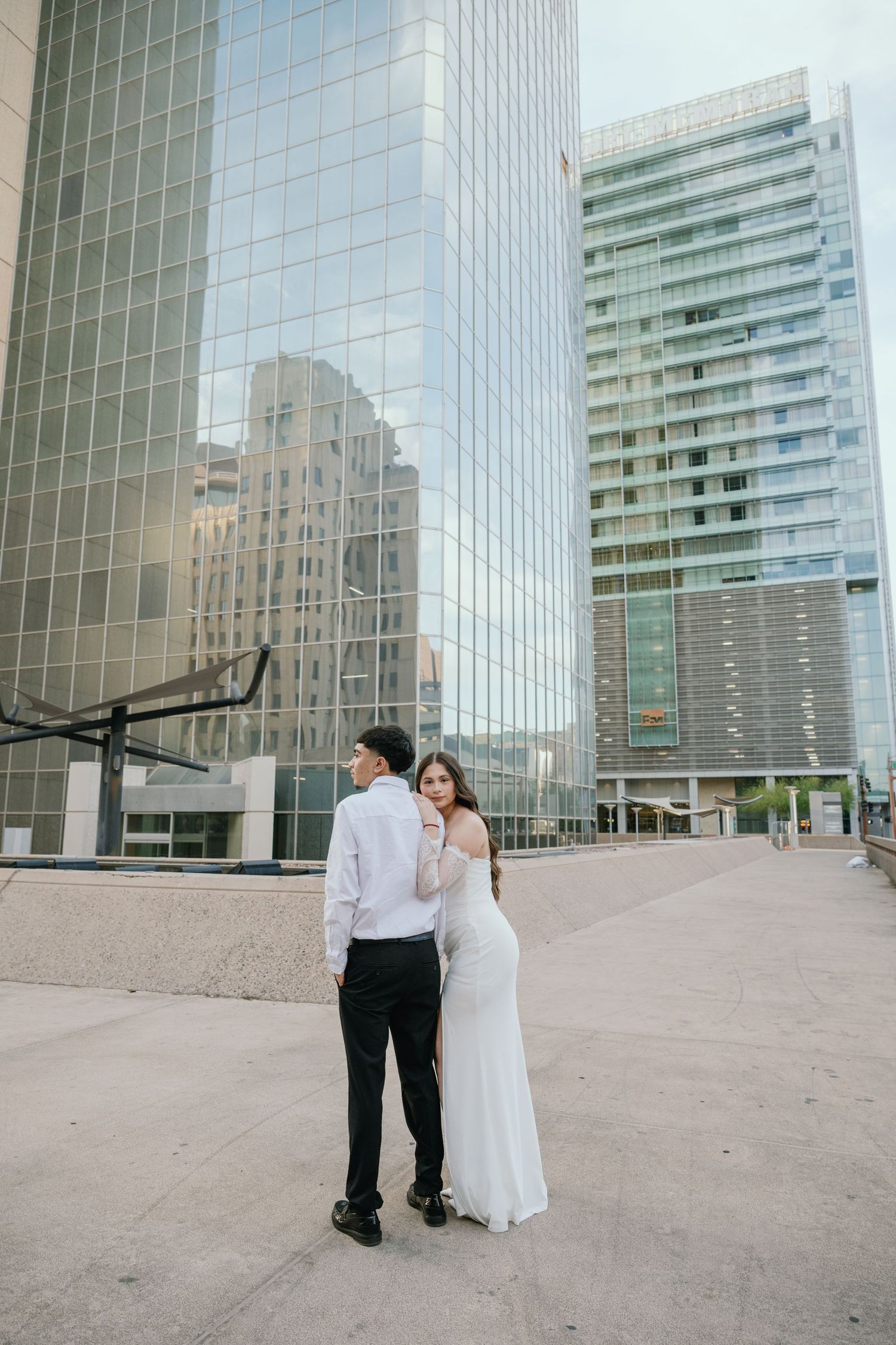 Newlyweds pose together against reflective glass buildings in downtown setting.