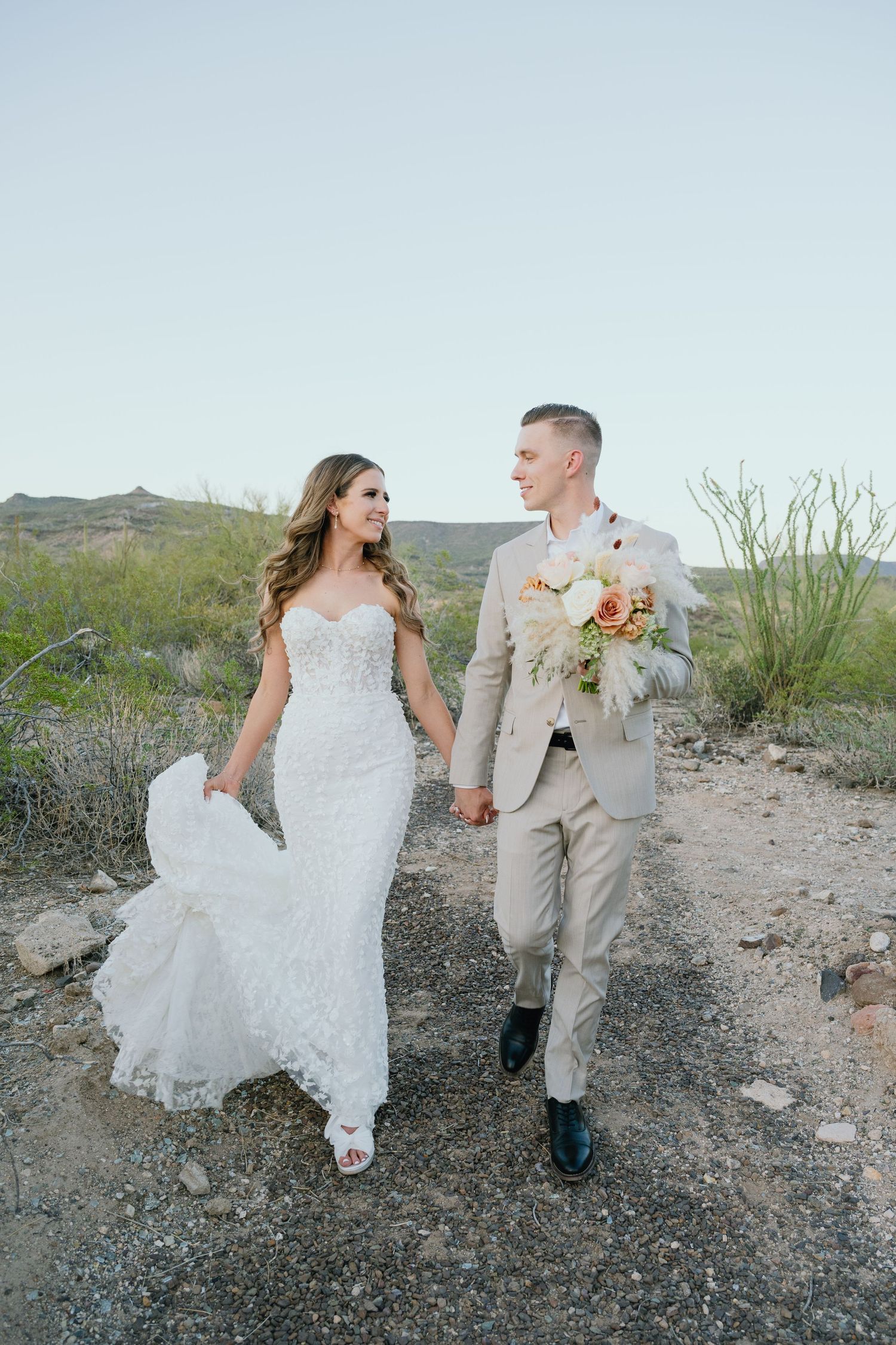 A happy wedding couple walking hand in hand through a desert landscape in formal attire.