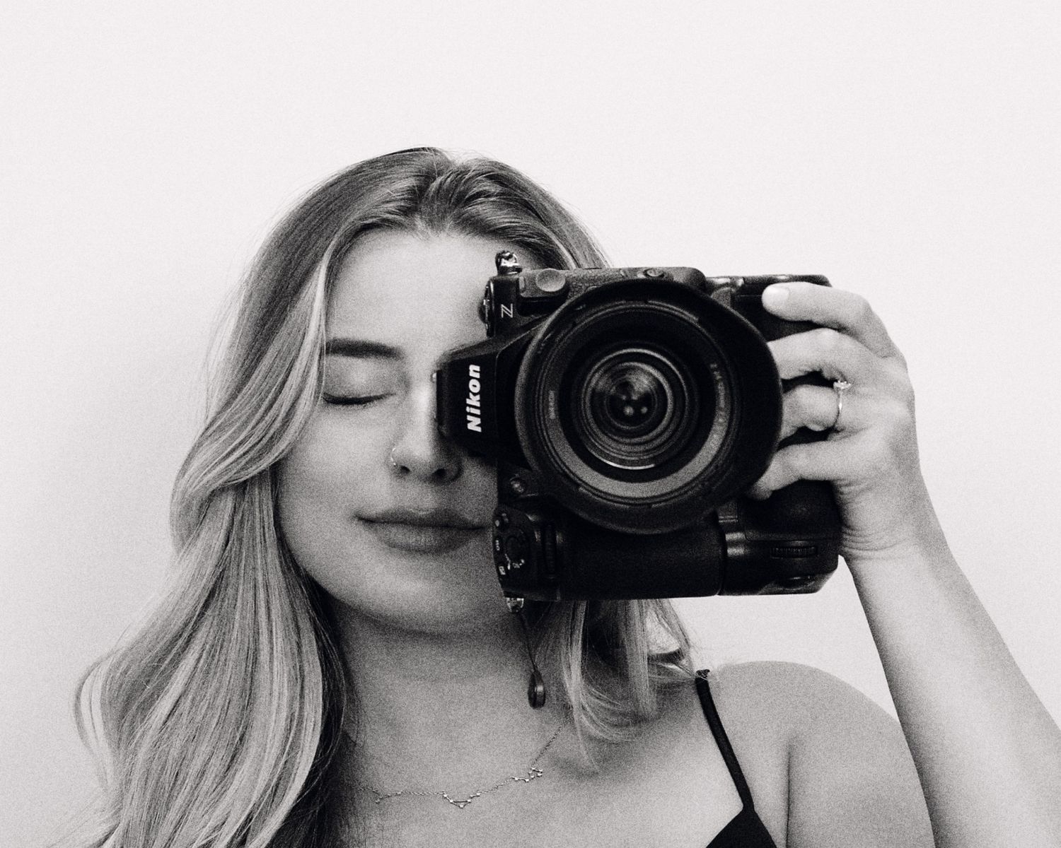 A black and white photograph of a photographer taking a self-portrait with a professional DSLR camera.