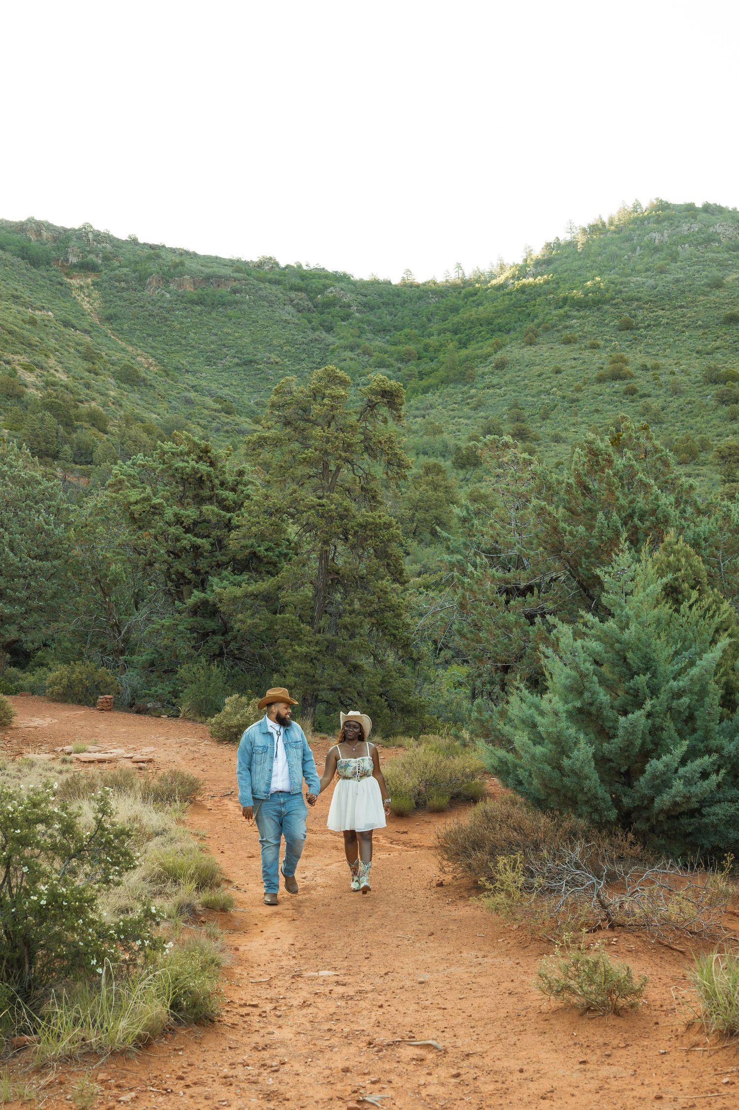 People walking together on a winding dirt trail through green hillside vegetation on a sunny day.