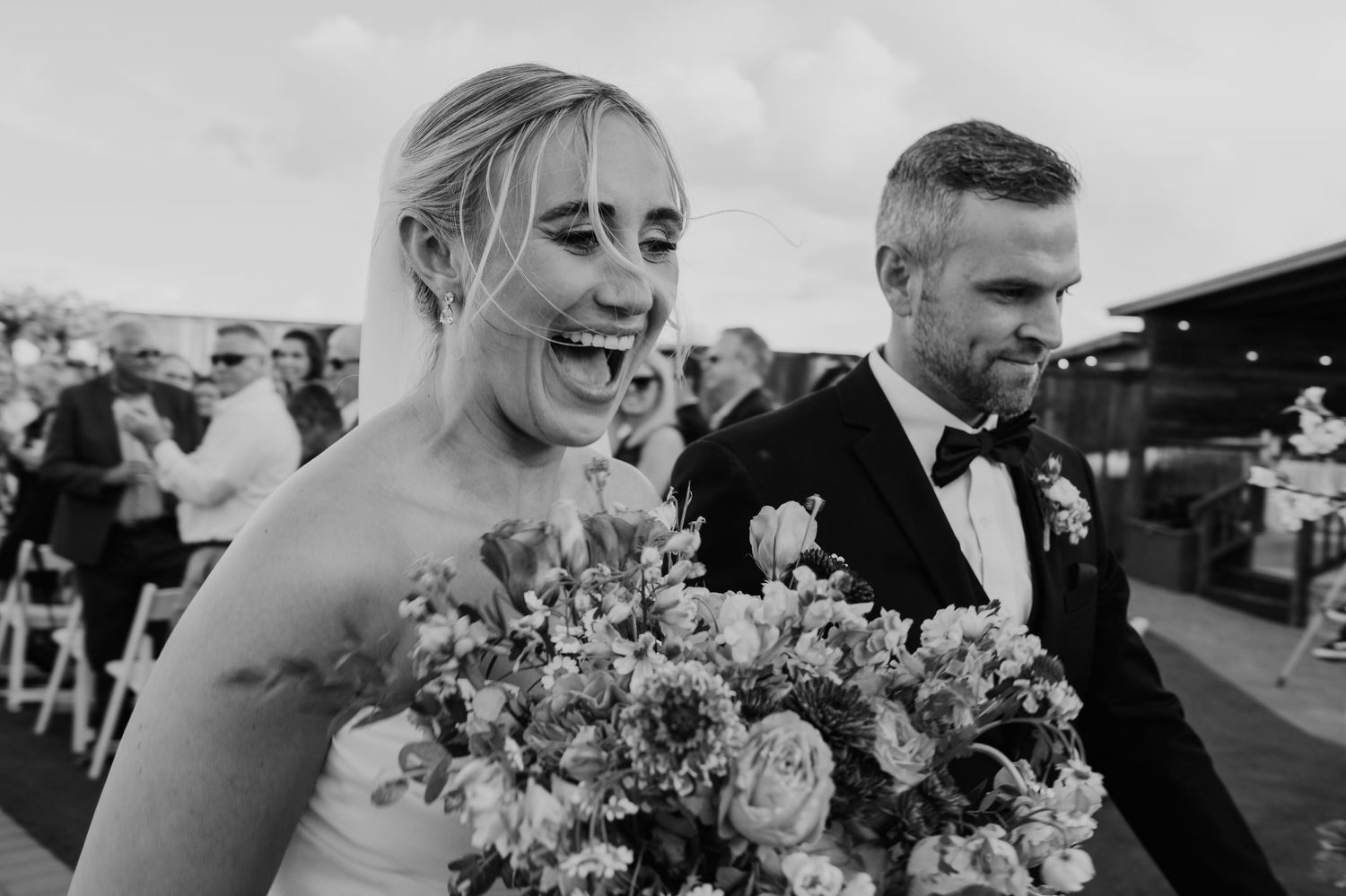 A joyful wedding couple walking together while the bride holds a vibrant purple and pink bouquet.