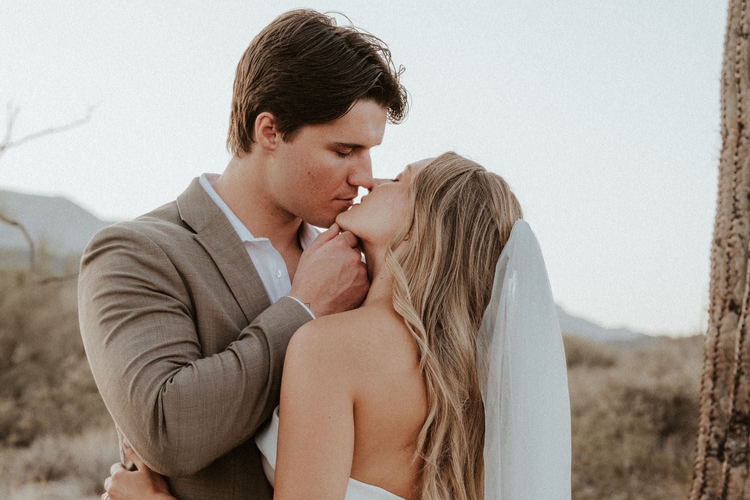 A romantic moment between newlyweds embracing outdoors in golden light with a scenic mountain backdrop.
