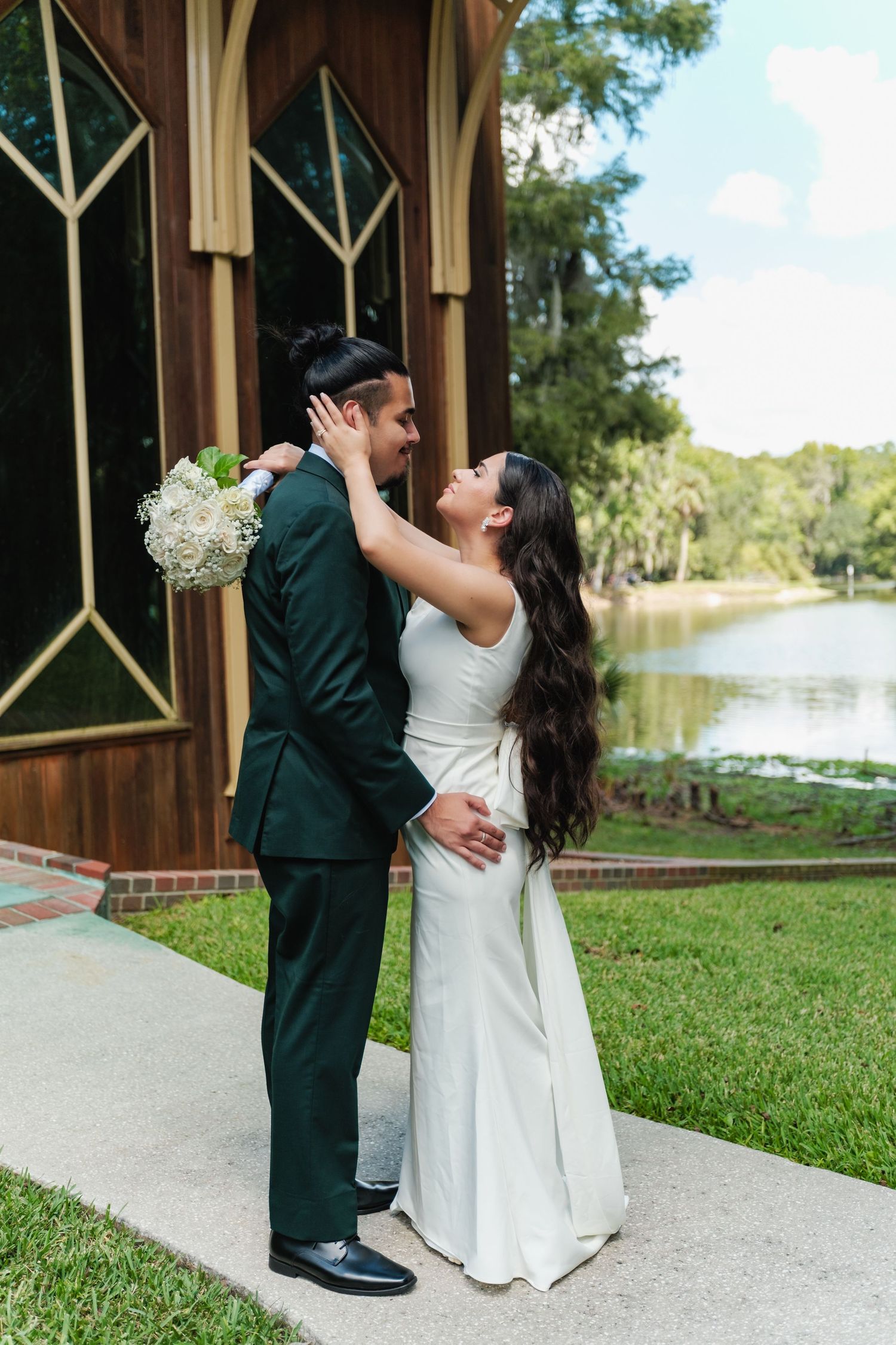 A romantic wedding photoshoot by a lakeside gazebo with a couple in formal attire embracing.