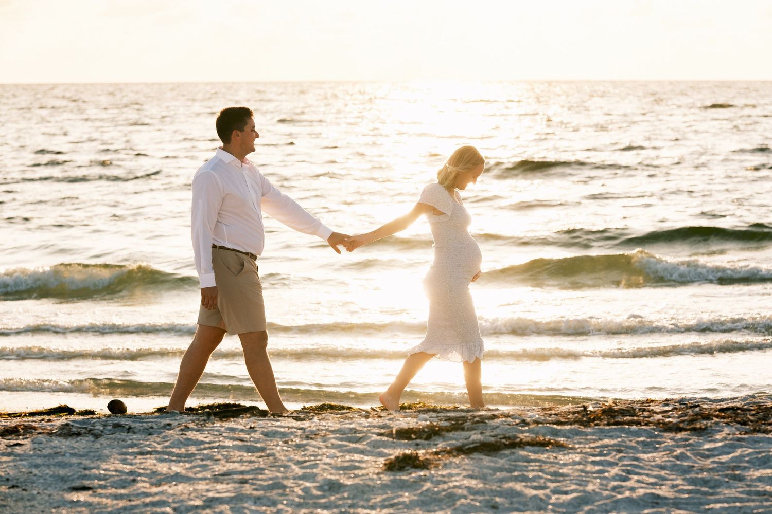 Romantic beach photoshoot at sunset with silhouettes walking along the shoreline.