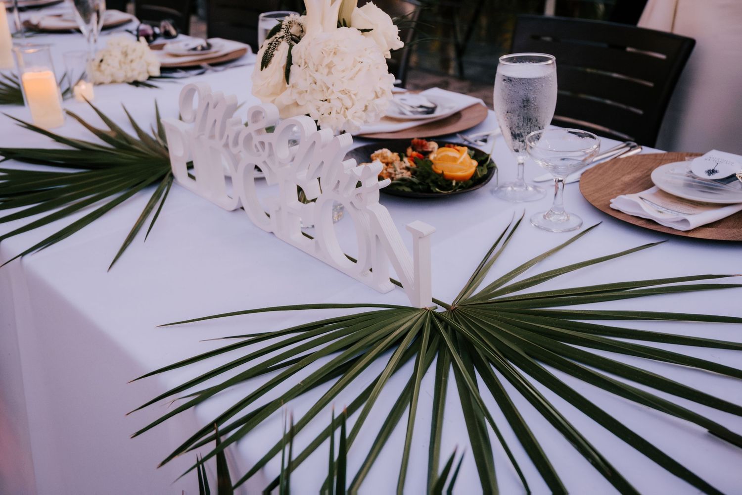 Wedding reception table settings with tropical palm leaves and elegant glassware.