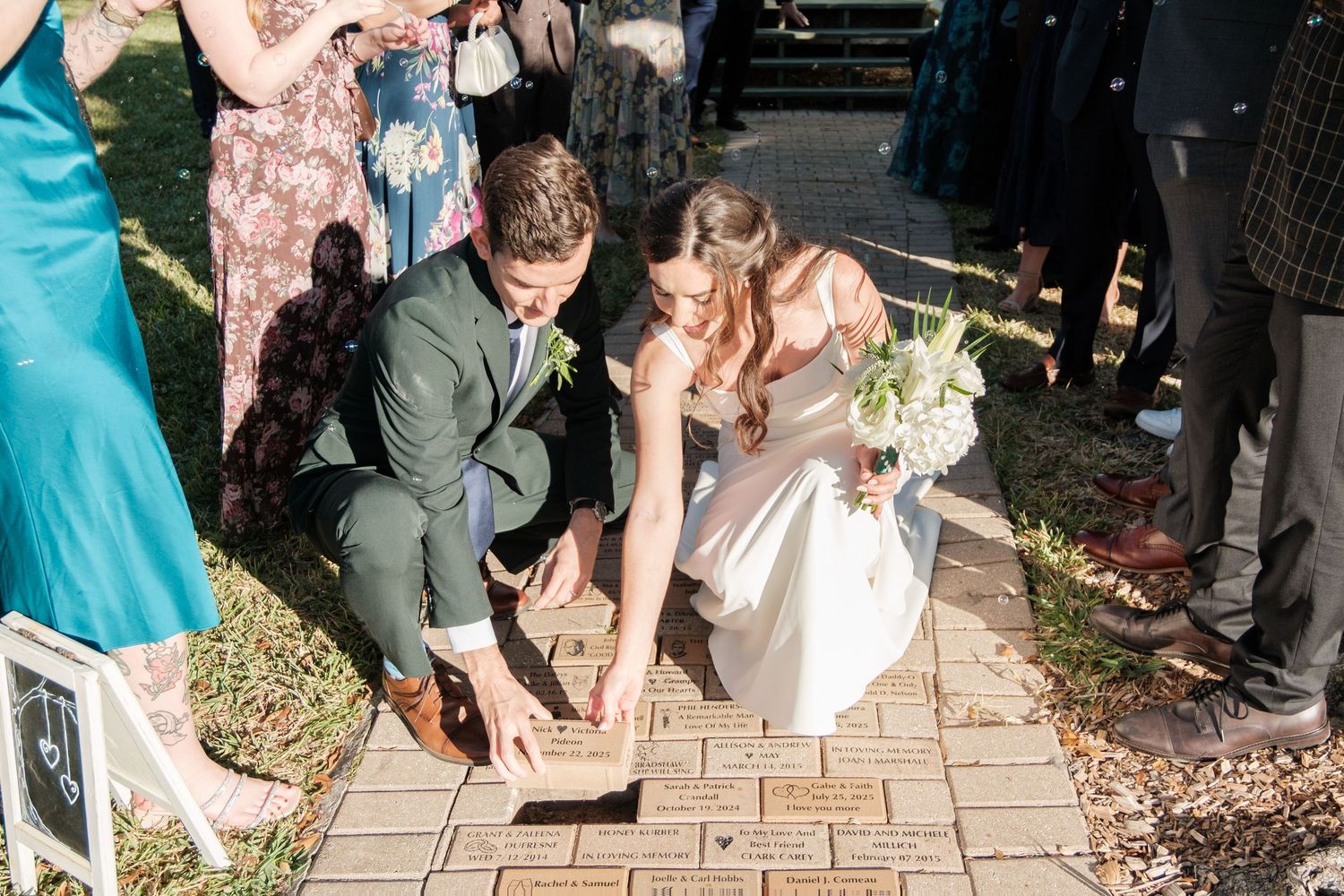 Wedding guests in colorful attire gather on outdoor steps during daytime celebration.