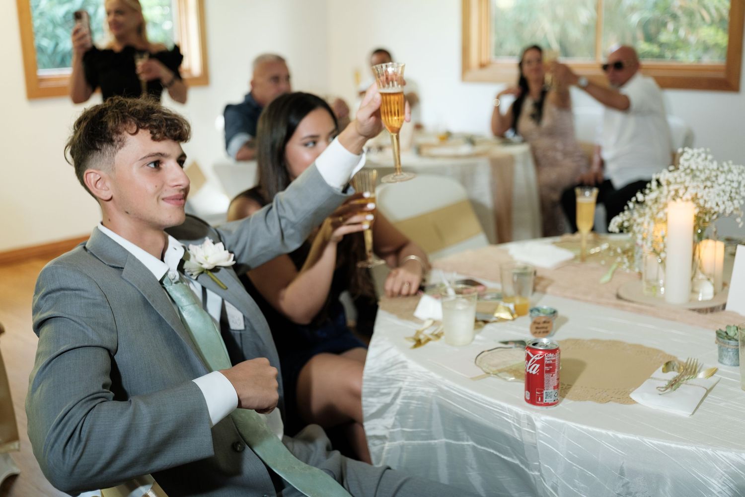 Wedding reception guests enjoying dinner and drinks at decorated tables in an indoor venue.