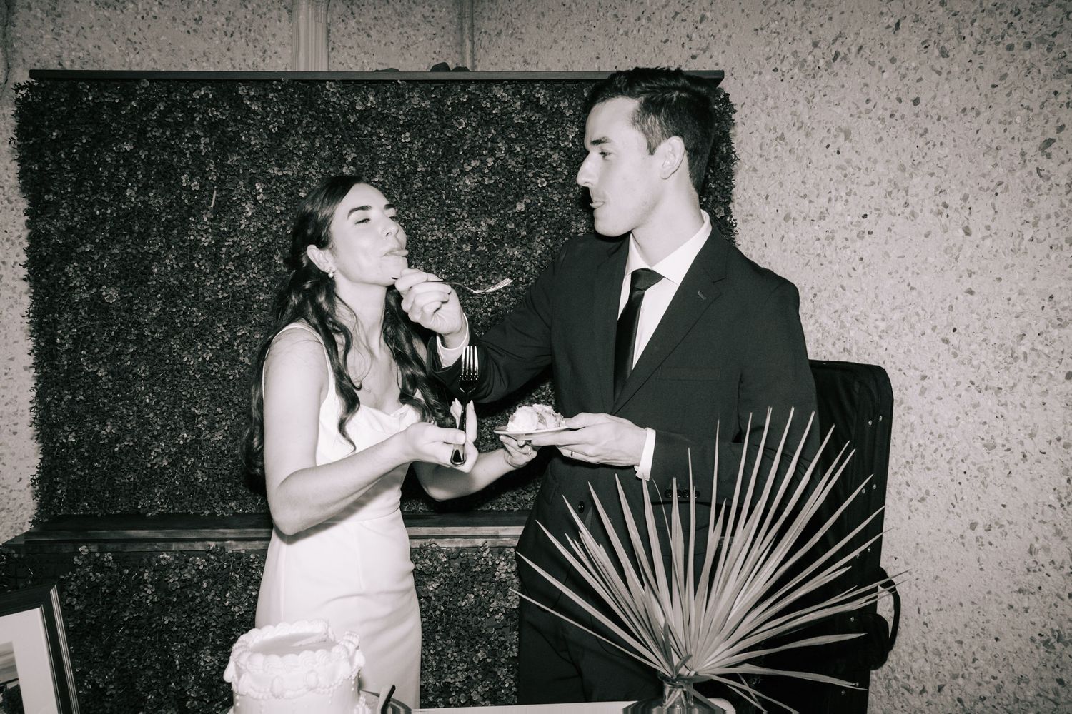 A black and white photo series showing a couple sharing cake at their wedding reception.