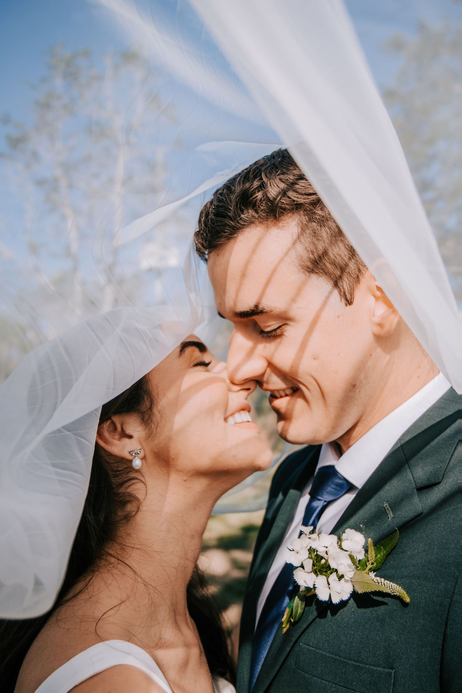 Close-up series of romantic wedding moments with flowing veil against blue sky.