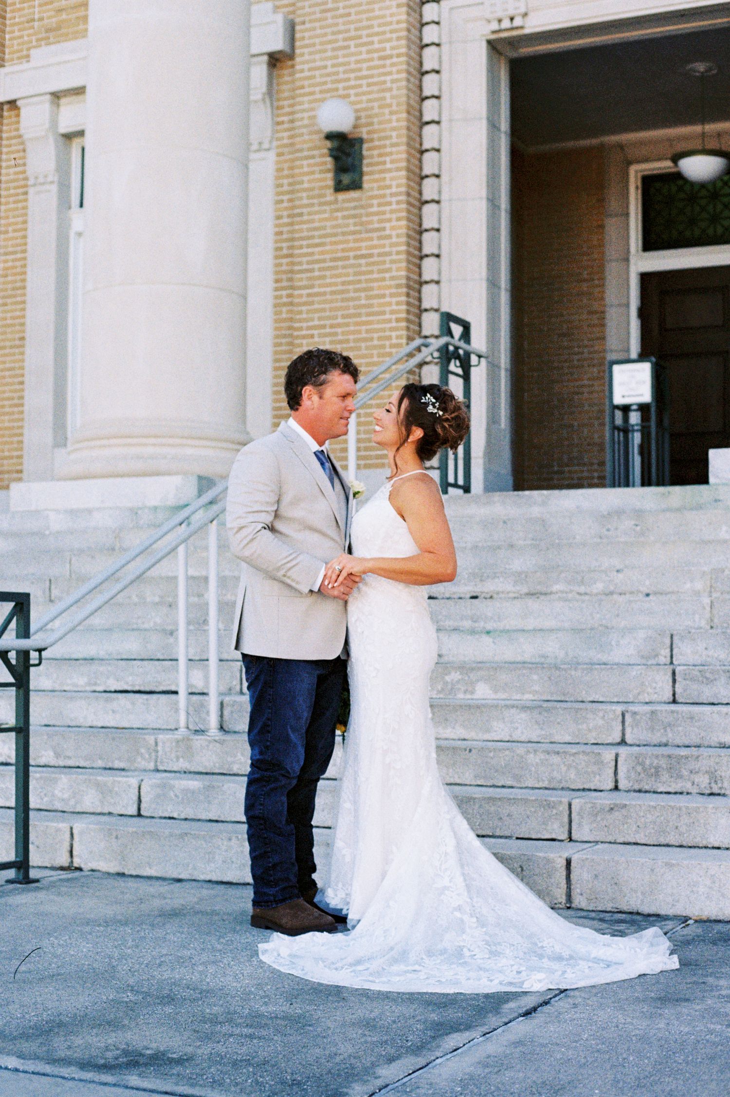 Bride and groom sharing a romantic moment on the steps of a classic stone building on their wedding day.