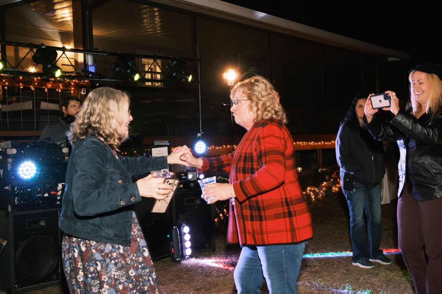 Two women dancing together at an outdoor nighttime event while a guest captures the moment on camera.