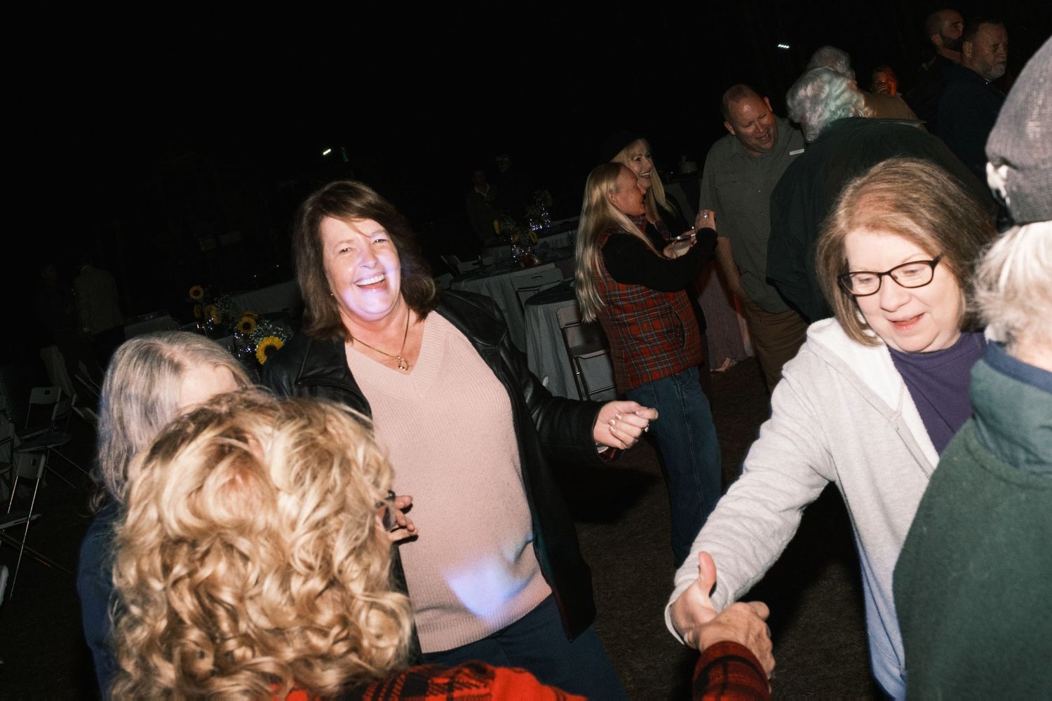 Two women laugh and dance joyfully together on the dance floor at an outdoor evening wedding reception.