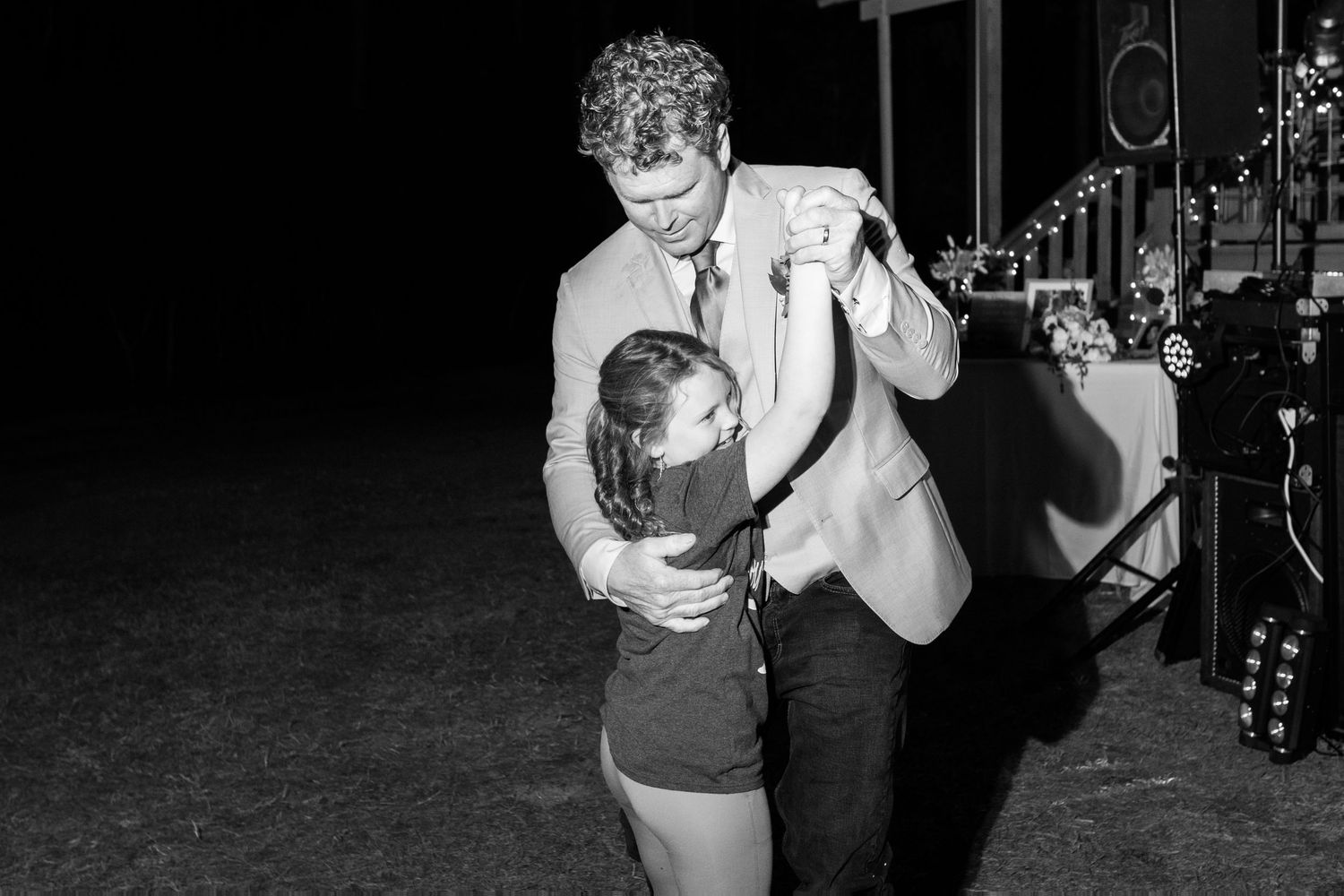 Black and white photo of a man in a suit dancing with a young girl at a reception.