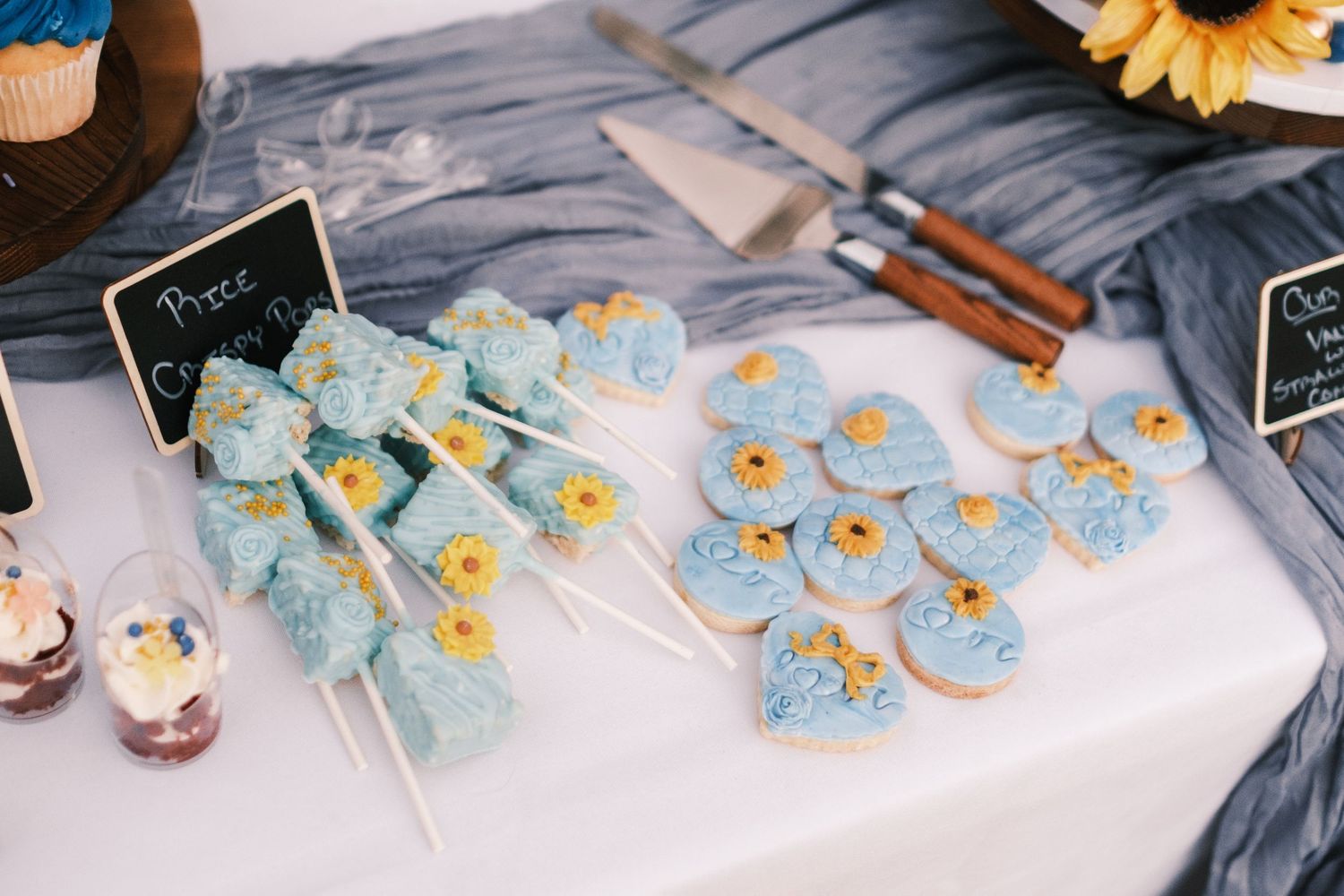 Blue and yellow sunflower-themed wedding dessert table with frosted cake pops and heart-shaped cookies.