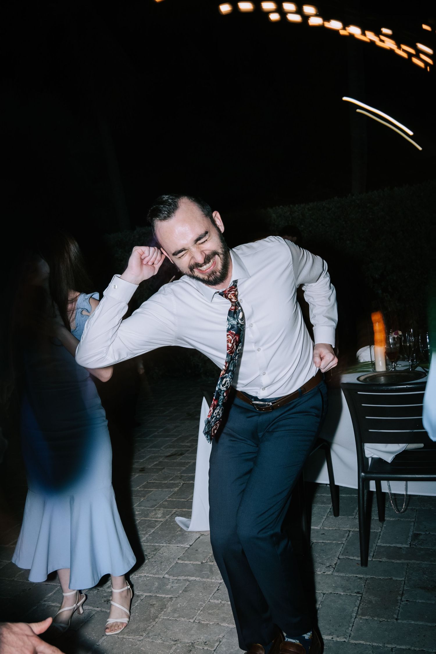 Wedding guests dancing energetically on stone floor under ambient lighting.