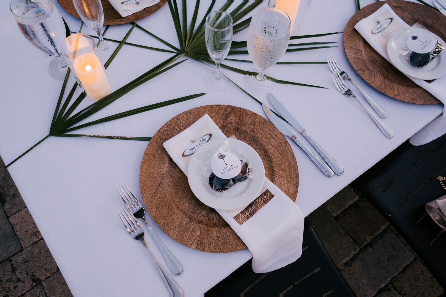 Wedding reception table settings with wooden chargers and tropical palm leaf decor.