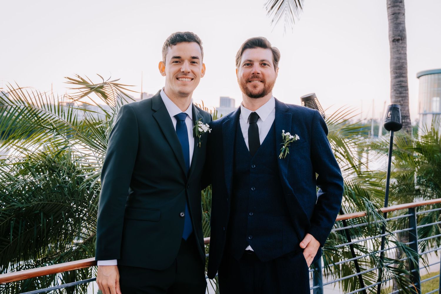 Groomsmen in navy suits pose together on tropical terrace with palm trees.