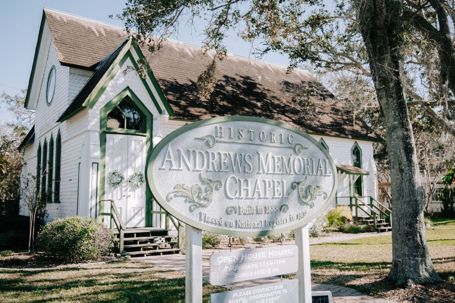 Historic white chapel buildings with green trim line a path under oak trees.