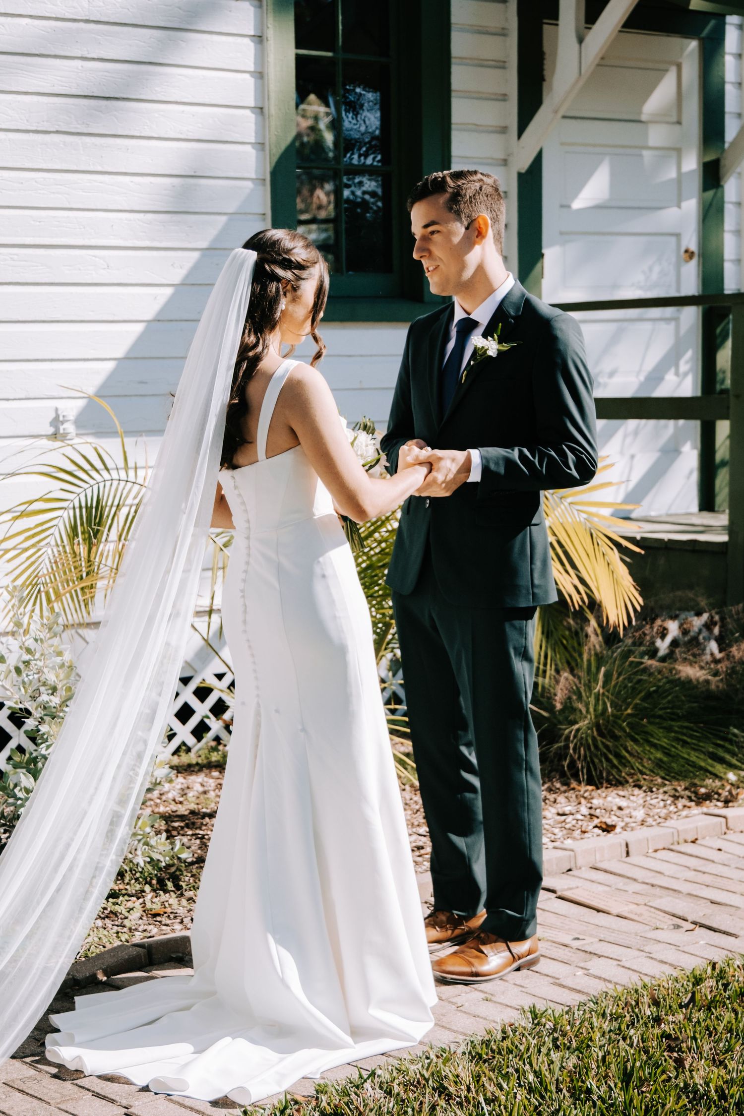 First look wedding photo sequence on white porch with palm trees and brick pathway.