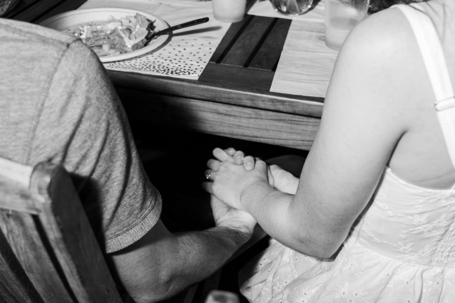 Black and white image of hands clasped in prayer during a religious service at a church pew.