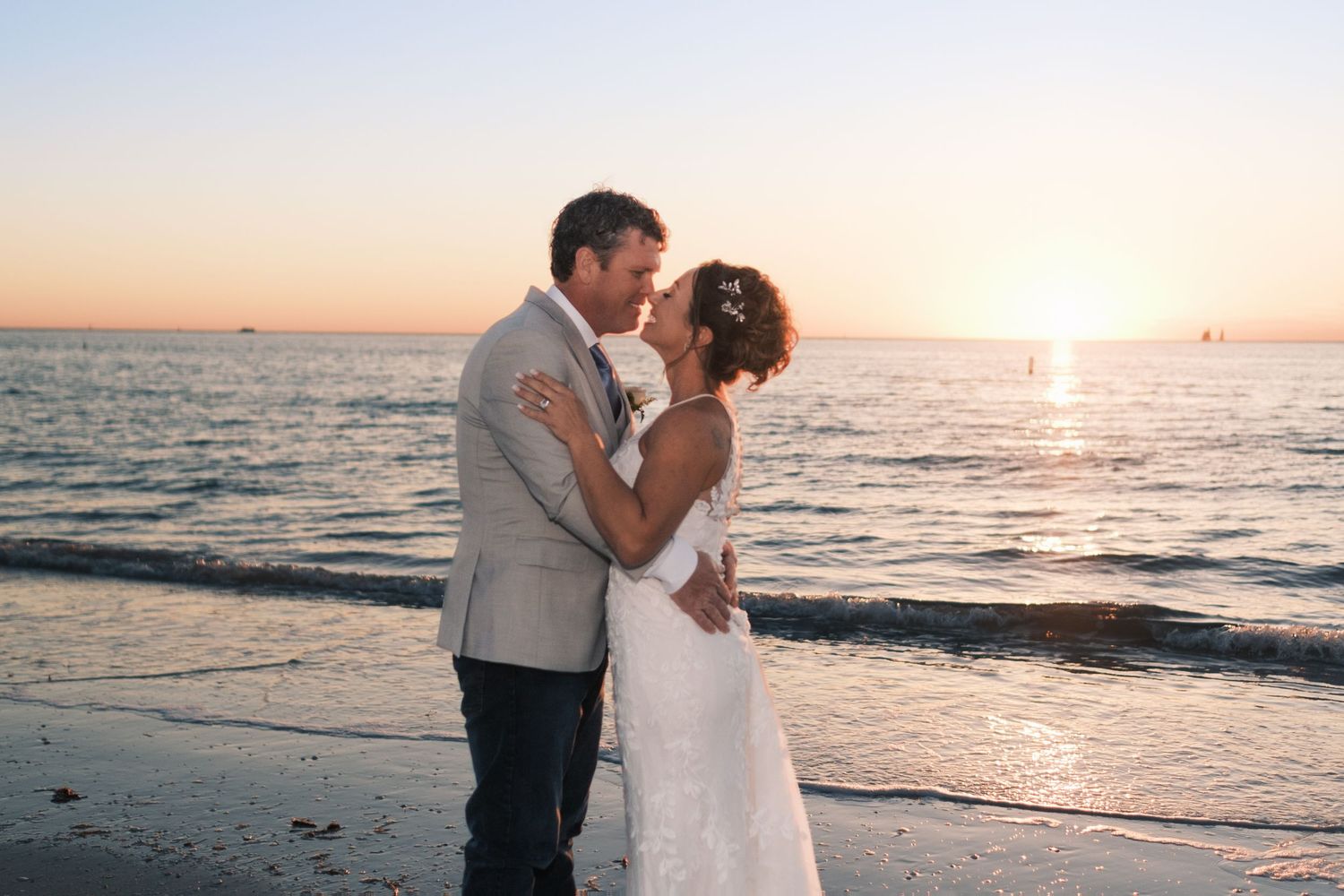 Bride and groom share a romantic kiss on the beach during a golden sunset over the ocean.