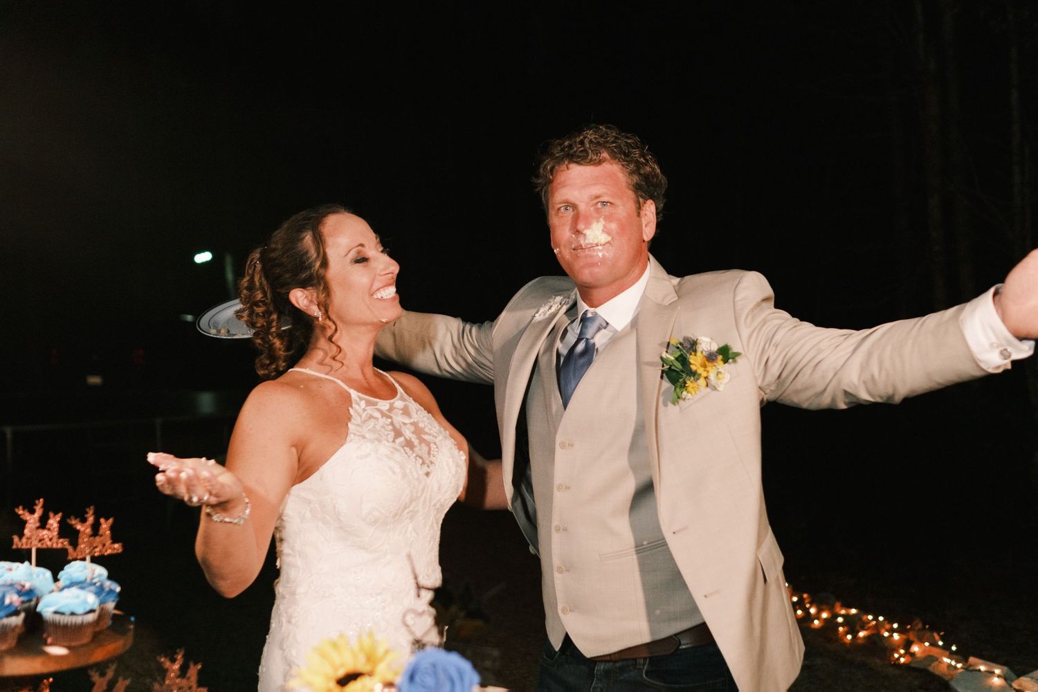 Bride and groom celebrate joyfully at their wedding reception with string lights and sunflower decorations nearby.