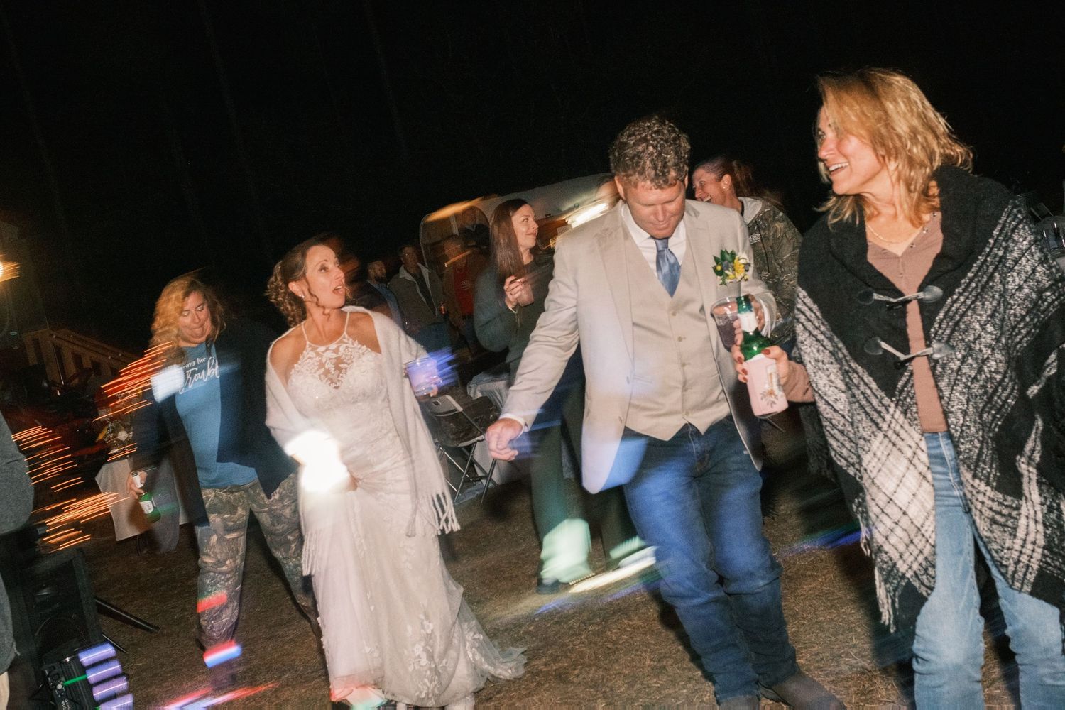 Bride and groom holding hands walking with guests at outdoor evening wedding celebration.