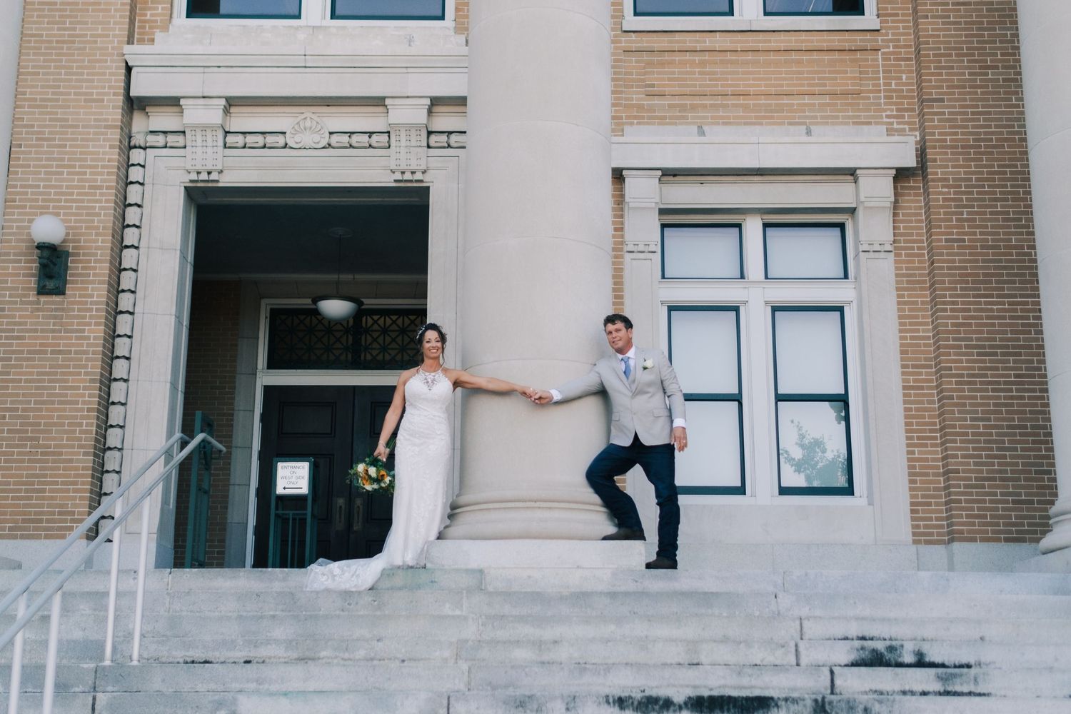 Bride and groom holding hands on steps of a brick building on their wedding day.