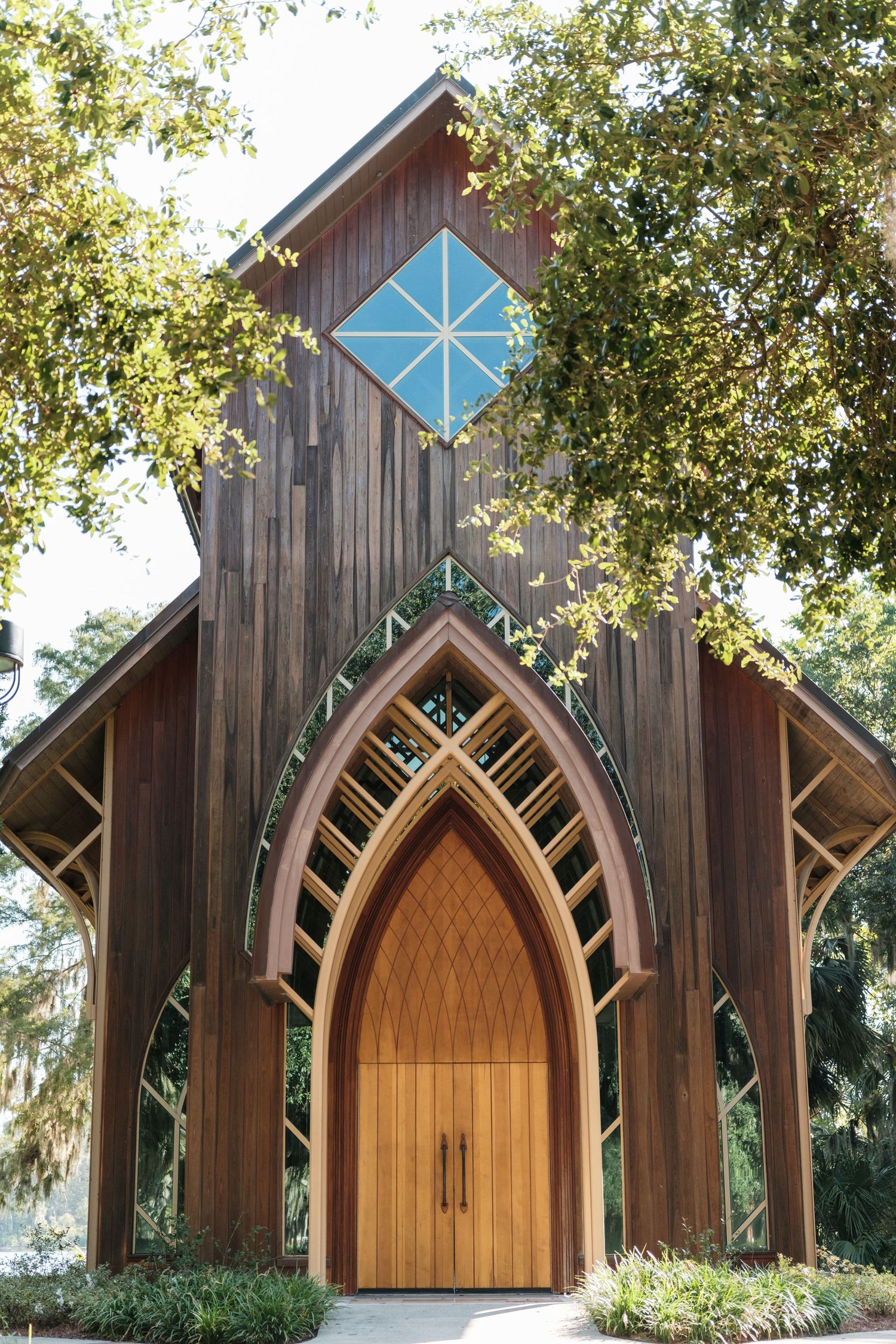 Exterior view of wooden chapel featuring geometric blue window and Gothic-inspired arched entrance.