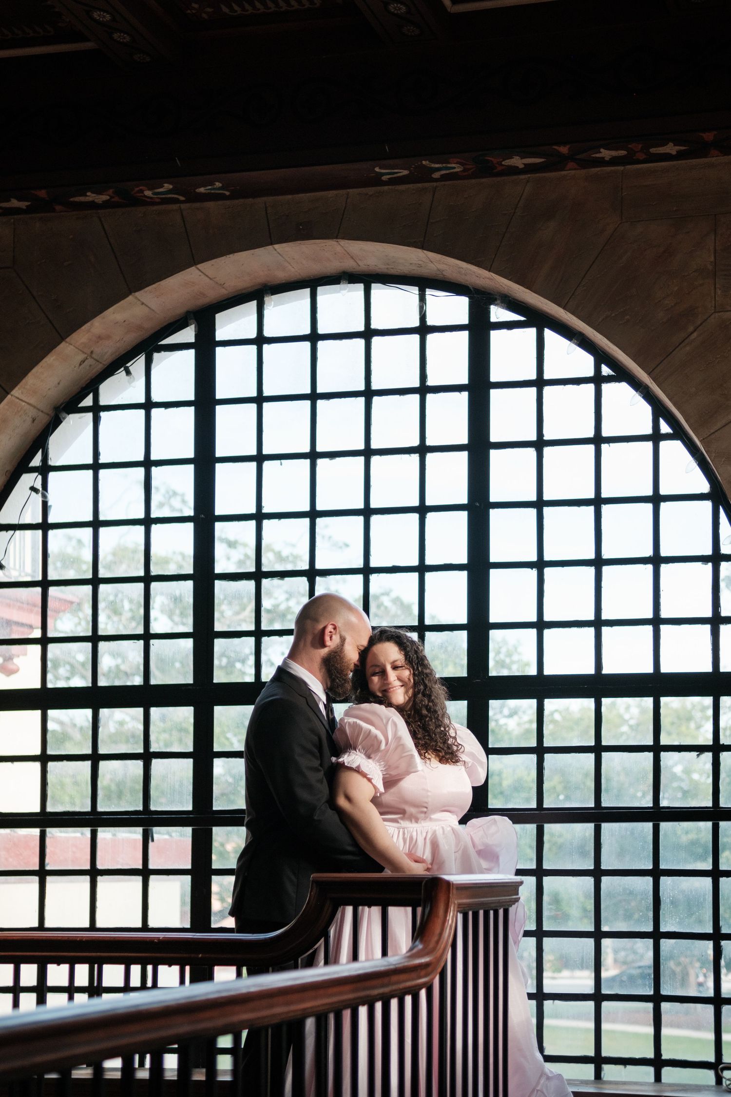 Couple shares romantic moment by arched window with scenic mountain view.