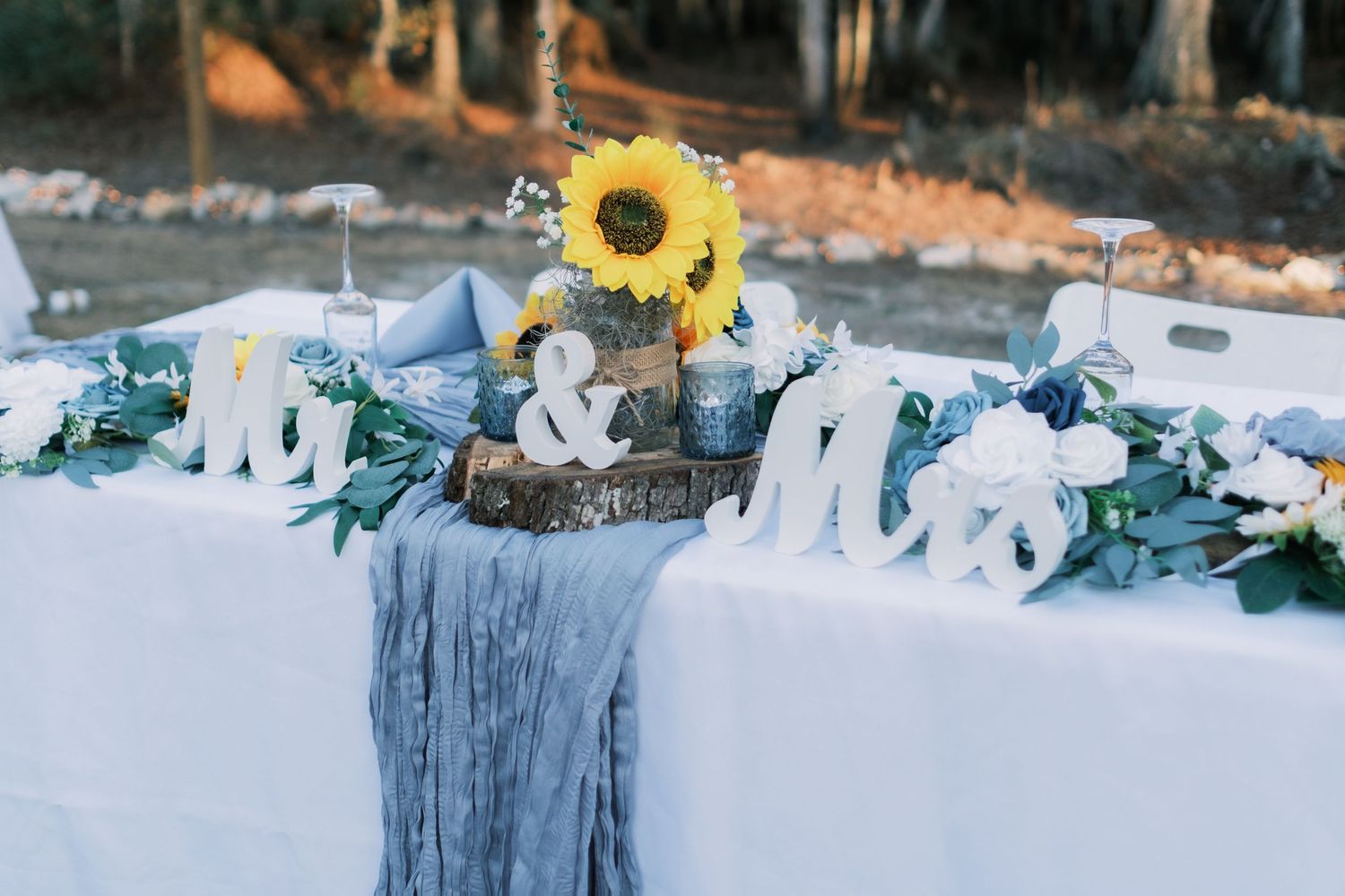 Sweetheart table with sunflower centerpiece, dusty blue runner, and MR MRS letters.