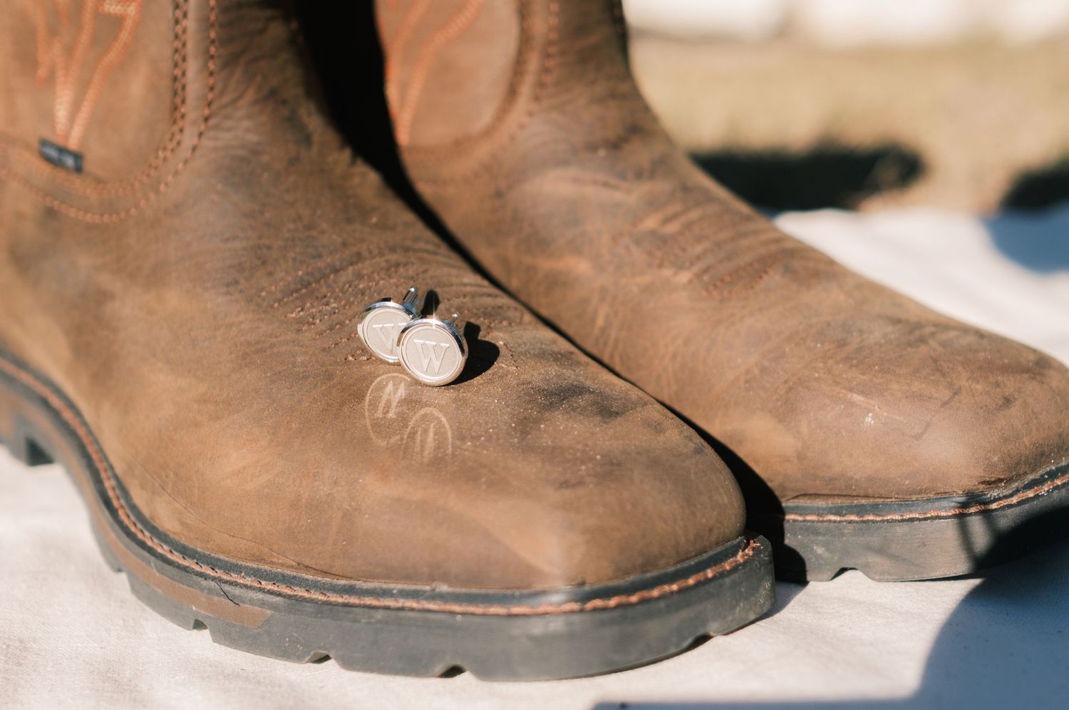 Close-up of worn brown leather cowboy boots with scuff marks resting on a white surface outdoors.